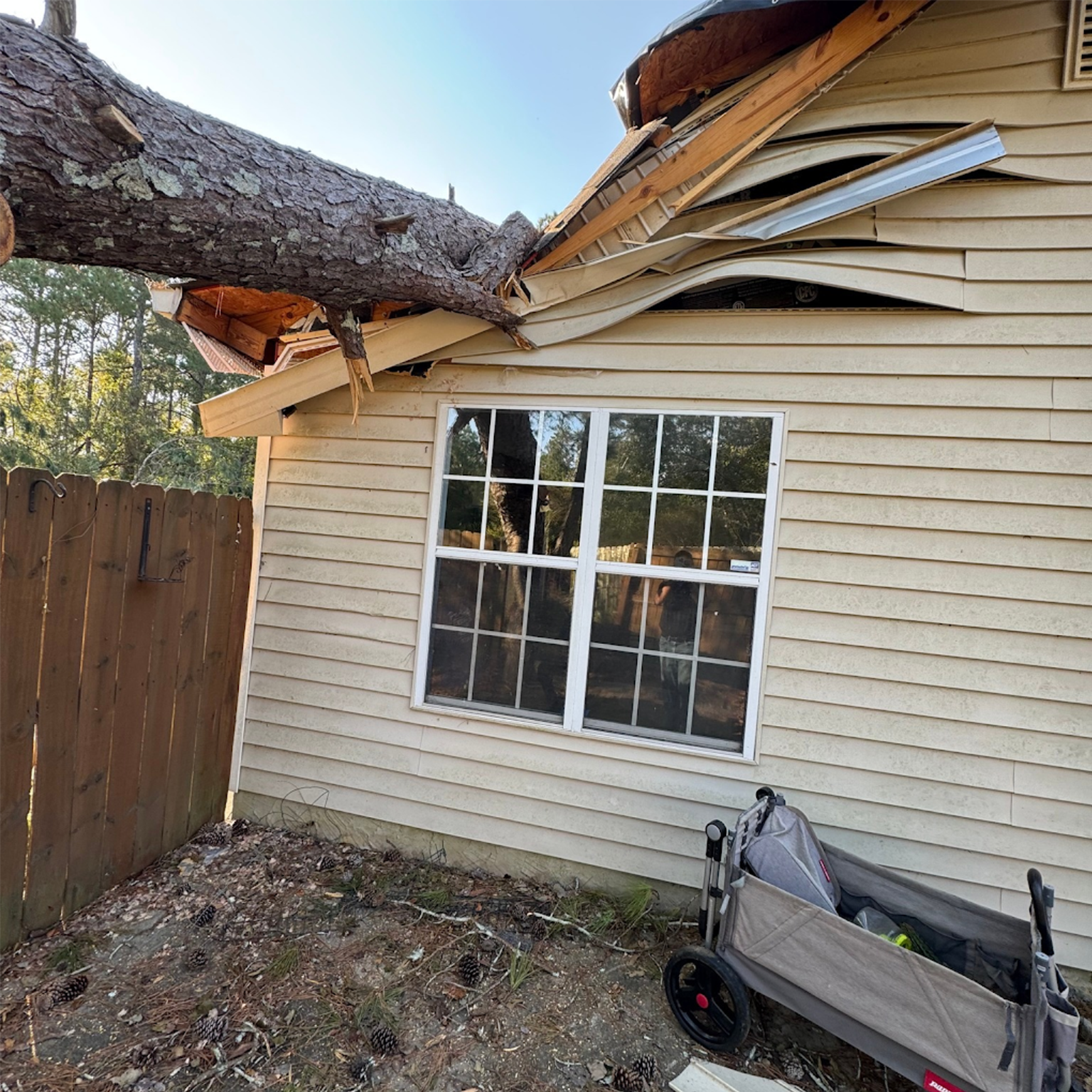 Storm-damaged roof and siding on a residential home with fallen tree debris.